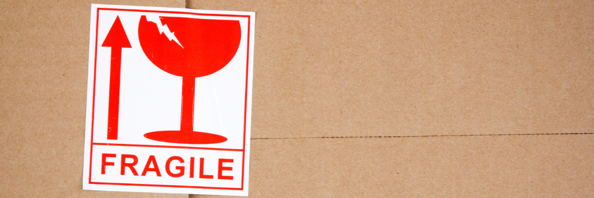 Hnedá kartónová krabica s nálepkou s textom fragile a obrázkom skleneného pohára a šípky hore